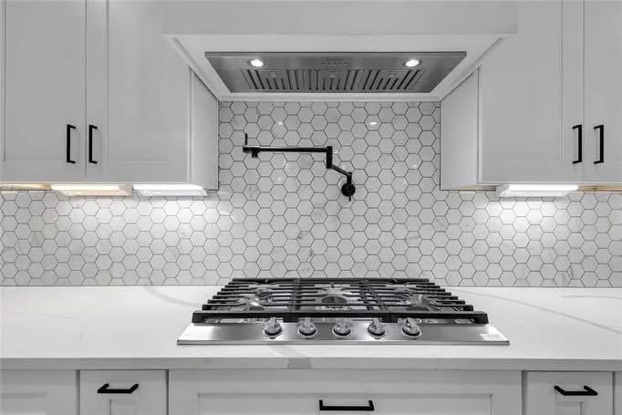 Gas range with white cabinetry and tile backsplash